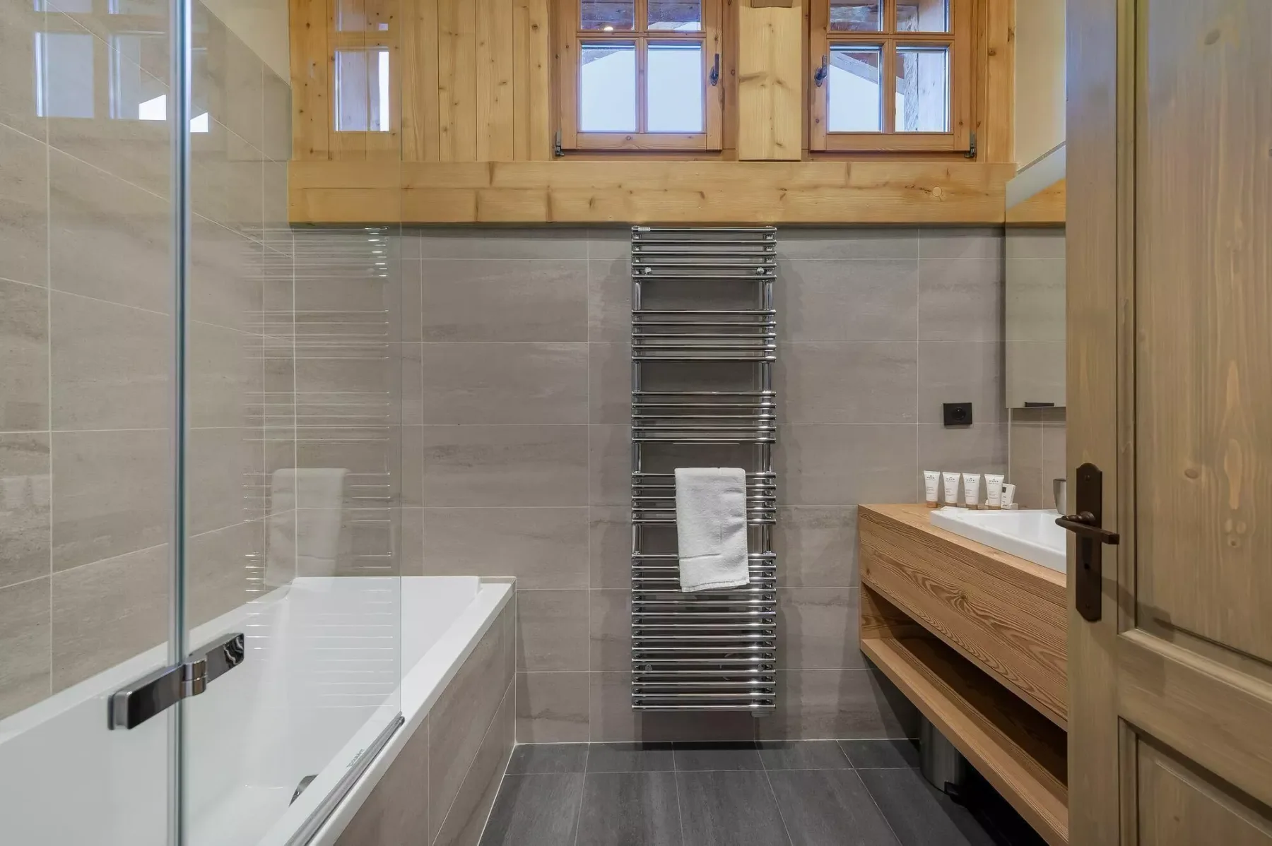 A bathroom with a bathtub, wooden vanity, and metal towel warmer.