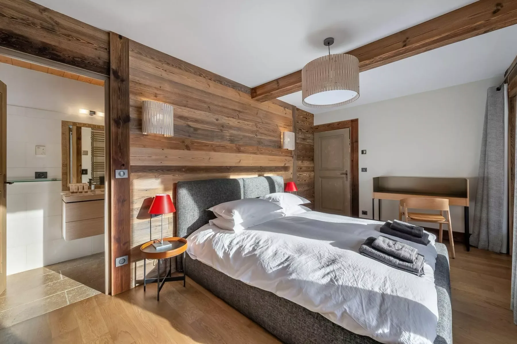 A bedroom with a neatly made bed, bedside tables, and a wood-paneled wall.