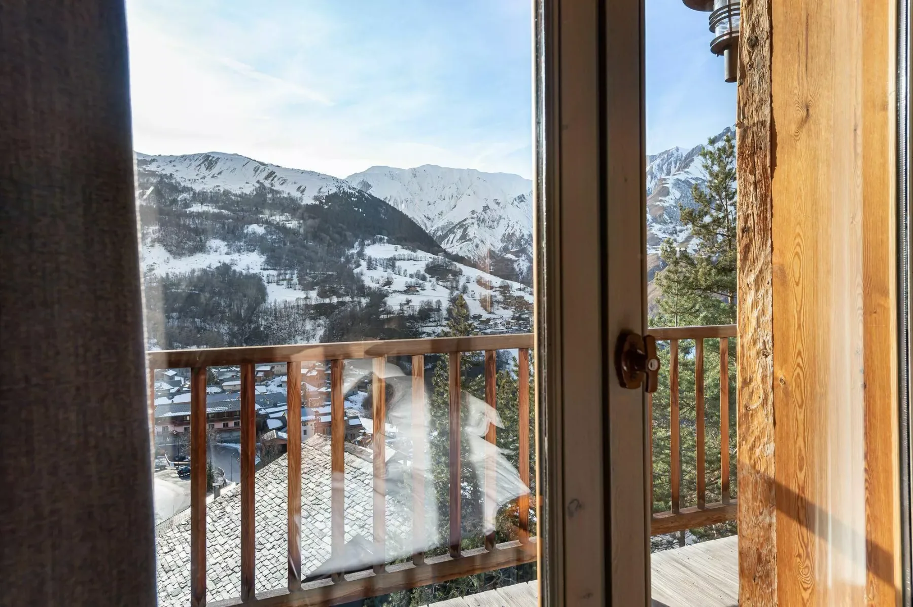A balcony overlooks a snow-covered mountain landscape through a glass door.