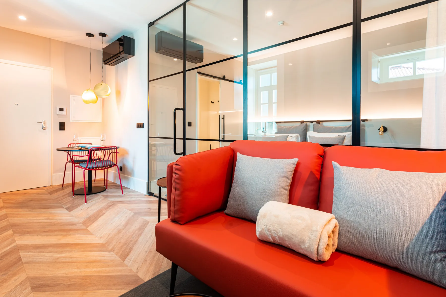 A living area with red seating and a glass partition opening onto a kitchen.