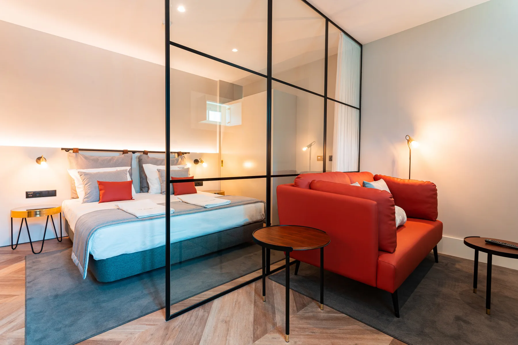 A bedroom and sitting area are divided by a black-framed glass partition.