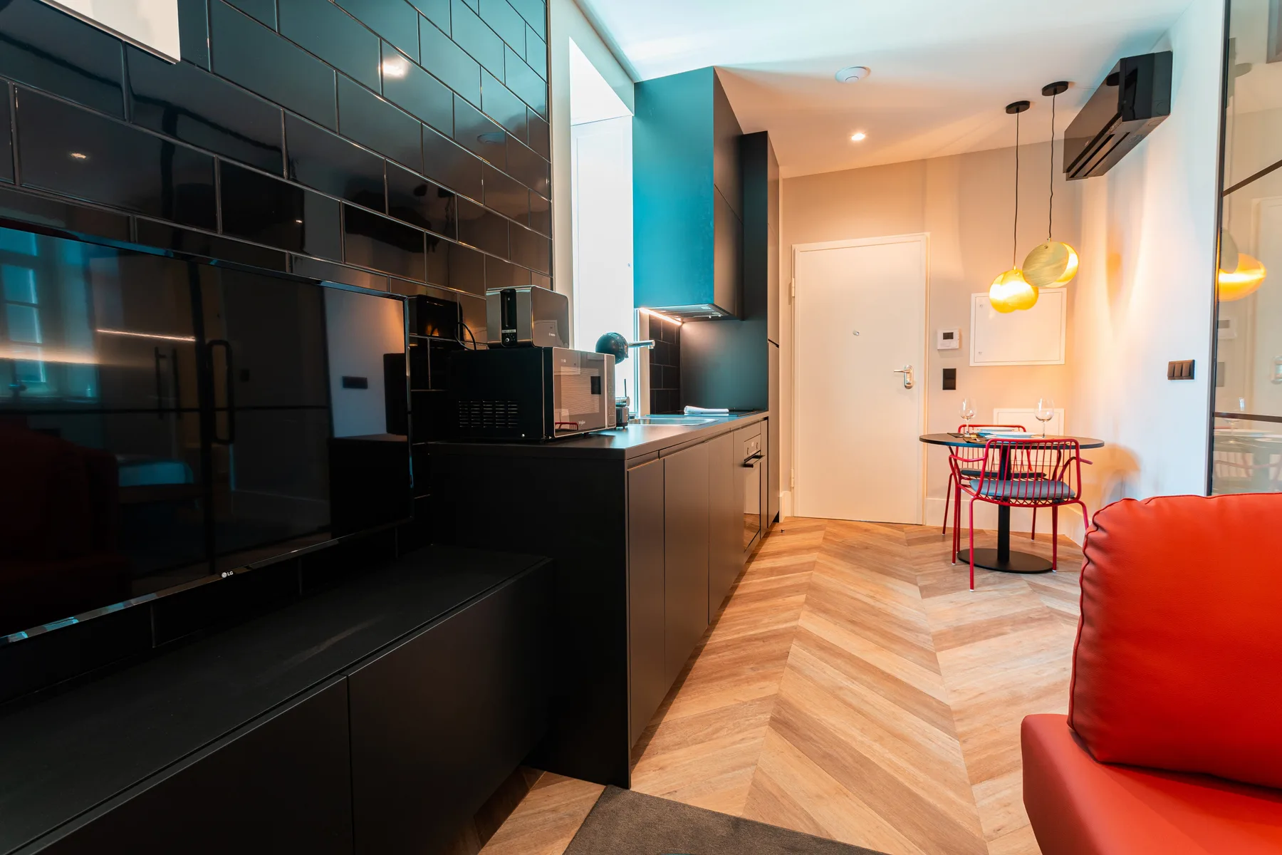 A modern kitchen opens into a dining area with a small table and red chairs.
