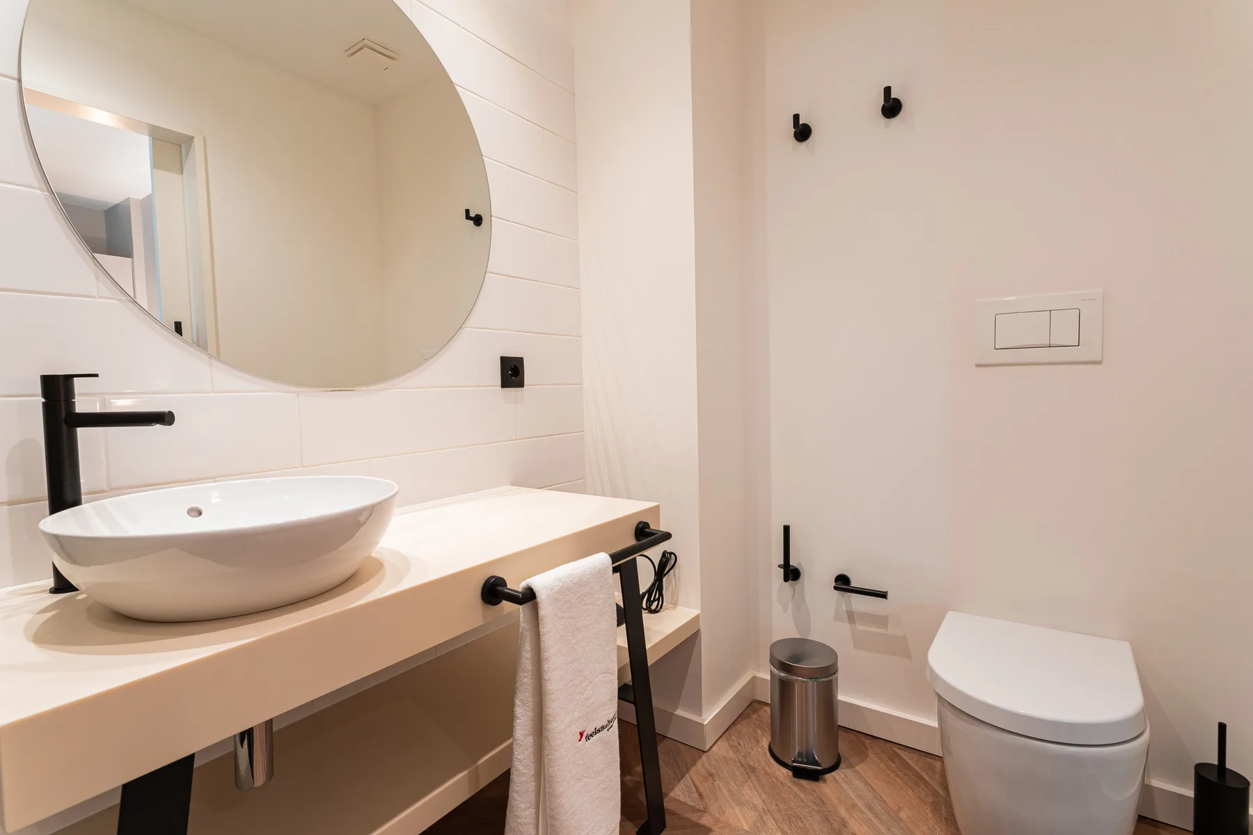 A bathroom with a sink, large round mirror, and toilet.