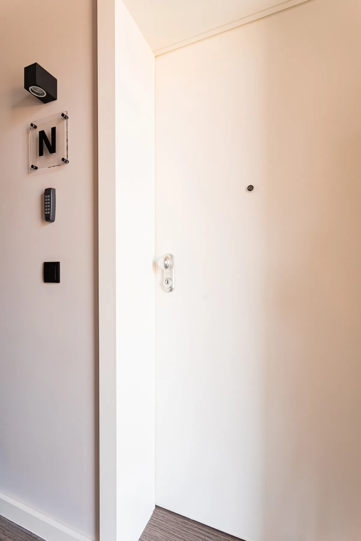 A white entry door with a peephole and wall-mounted controls.