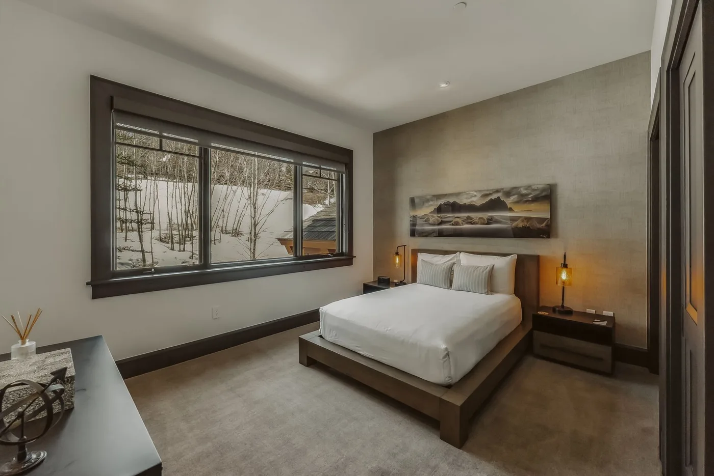 Un dormitorio con una cama bajo un cuadro y una ventana amplia con vista a árboles.