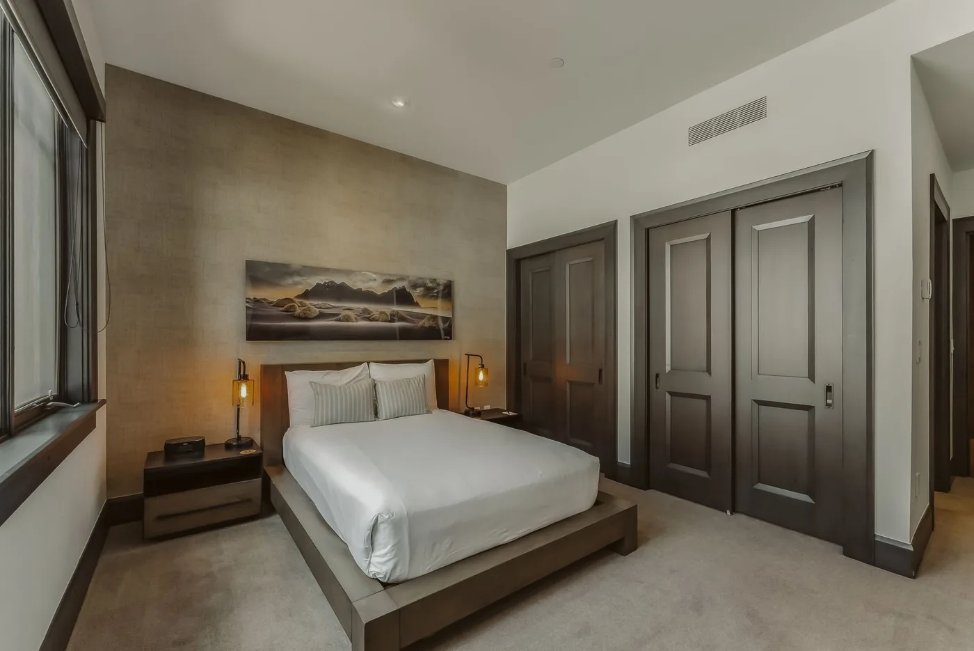 Un dormitorio con una cama bien tendida, mesas de noche y un cuadro en la pared.