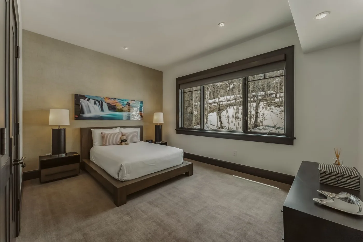 Un dormitorio con una cama junto a una gran ventana con vista a los árboles.