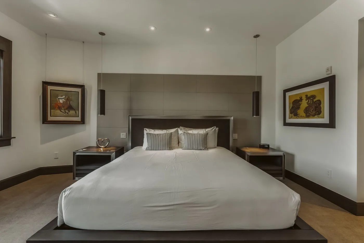 Un dormitorio con una cama grande, mesitas de noche y cuadros en las paredes.