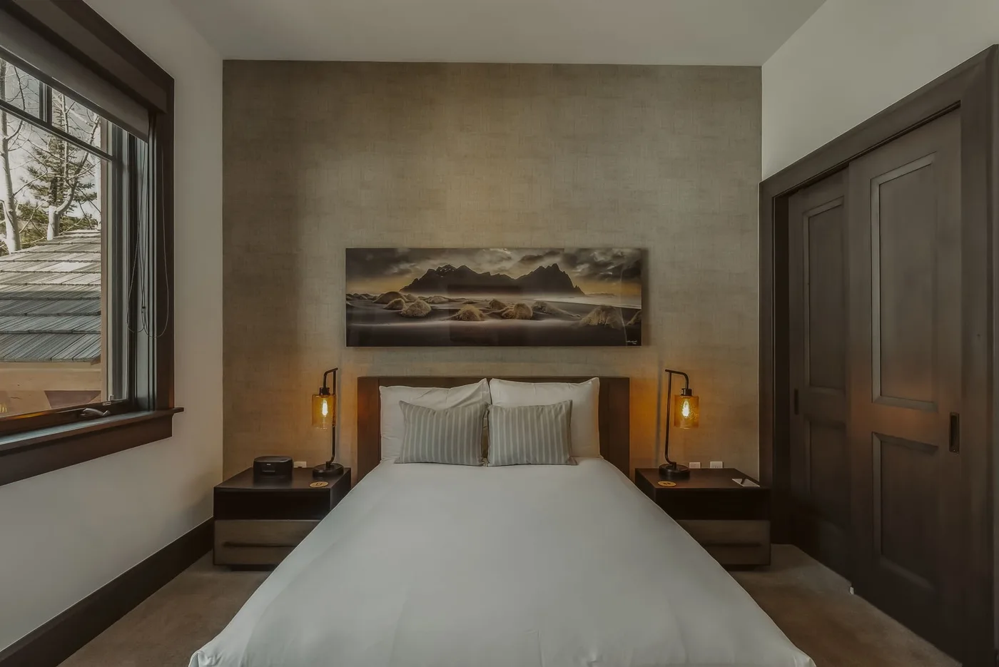 Un dormitorio con una cama bien tendida y un cuadro de paisaje sobre el cabecero.