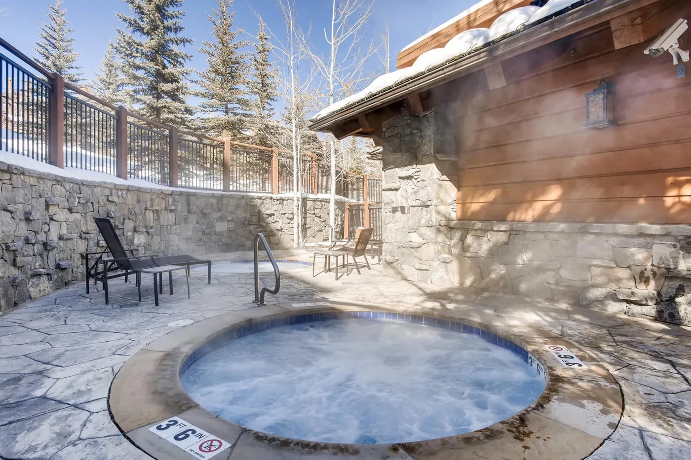 Una bañera de hidromasaje exterior está en un patio de piedra junto a un edificio de madera.