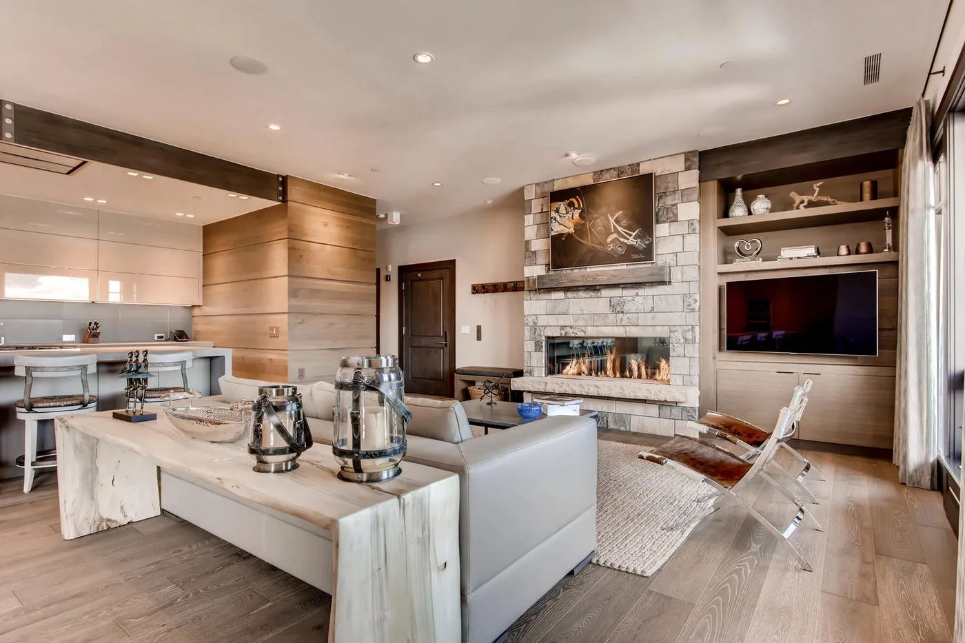 Sala de estar y cocina de concepto abierto con chimenea de piedra y televisor empotrado.