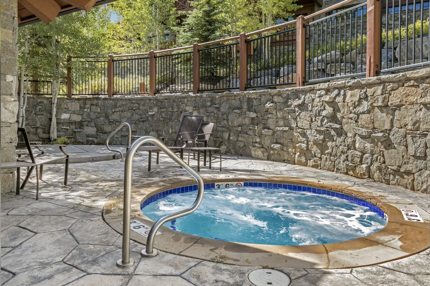 A bubbling hot tub sits on a stone patio beside a stone retaining wall.