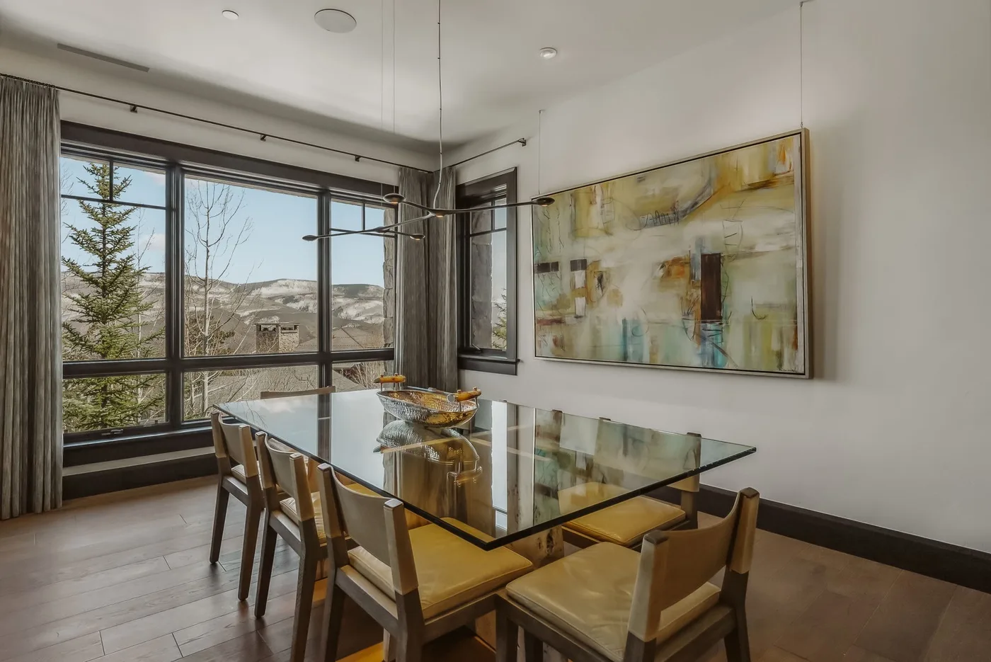 Comedor con mesa de vidrio y grandes ventanas con vistas al paisaje.