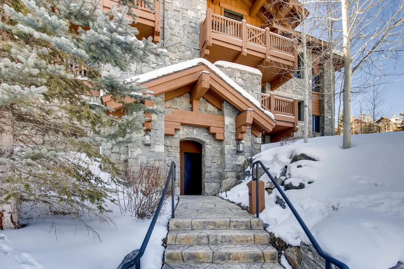 Entrada de un edificio de piedra con escaleras y balcones de madera, rodeada de nieve.