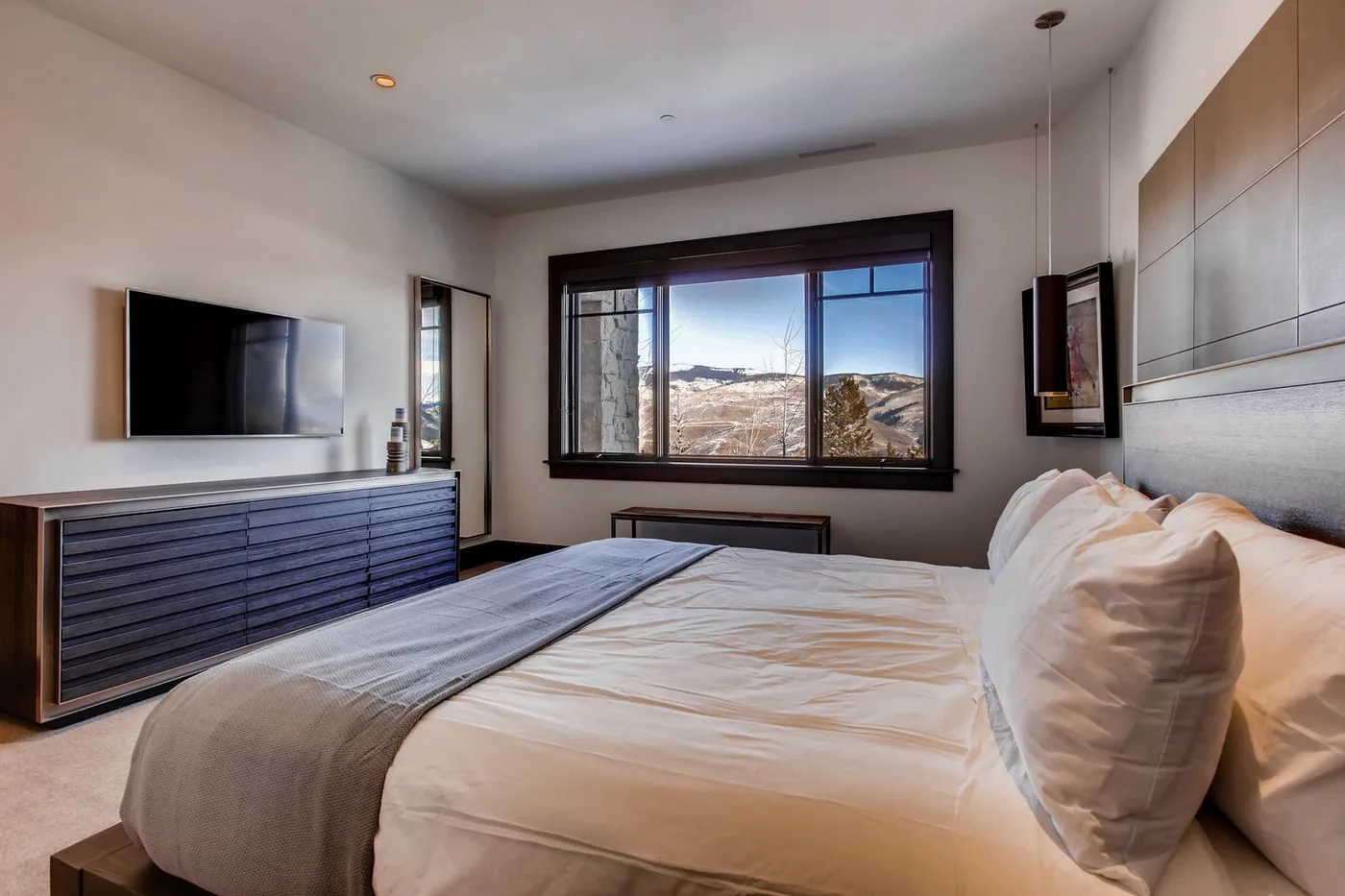 Un dormitorio con una cama grande frente a una amplia ventana con vistas a las colinas.