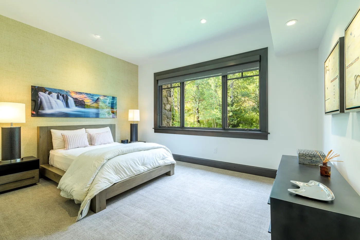 Un dormitorio luminoso con una cama junto a una amplia ventana con vistas a la vegetación.