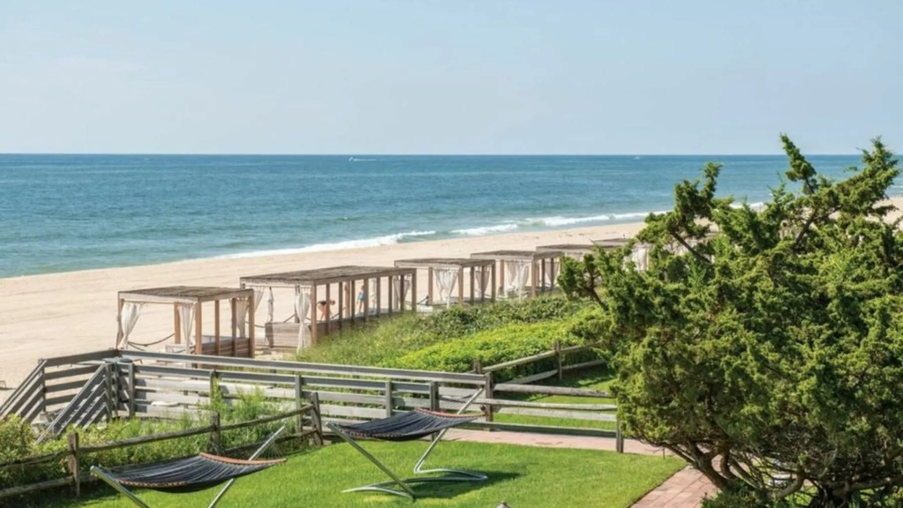A seaside lawn overlooks the beach, with hammocks and shaded seating near the dunes.