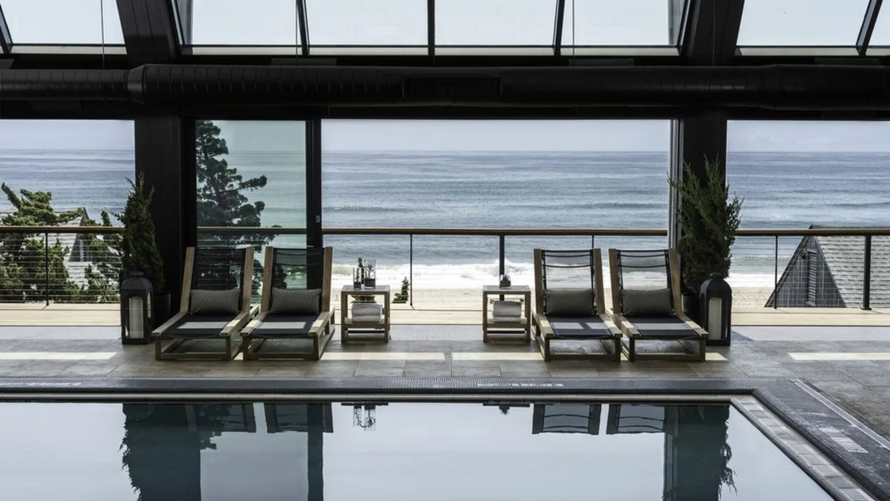An indoor pool overlooks the ocean through large glass windows.