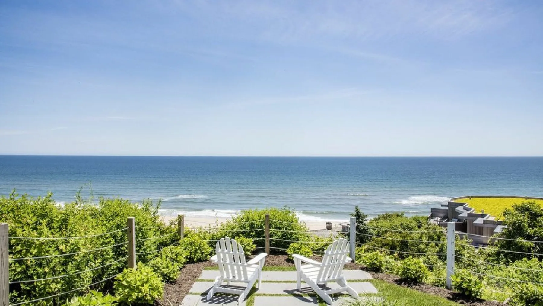 An outdoor seating area overlooks the ocean, with greenery along the edge.