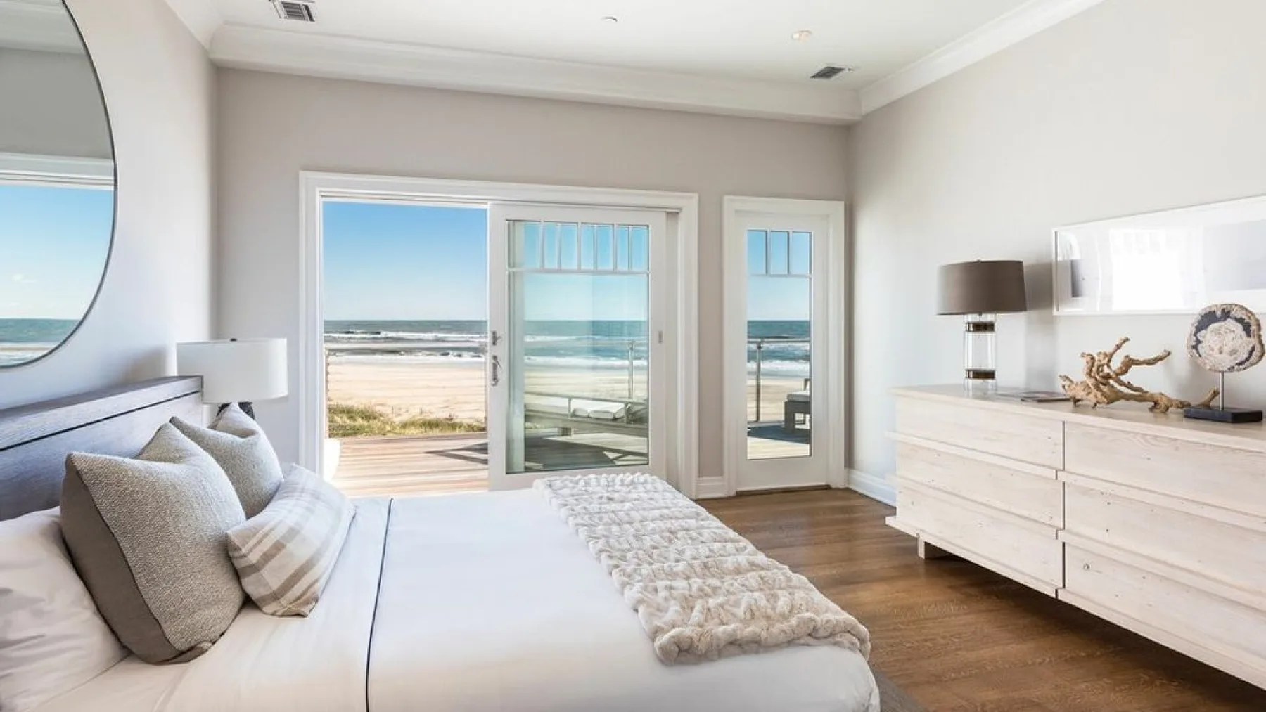 A bright bedroom with a bed beside large glass doors overlooking the ocean.