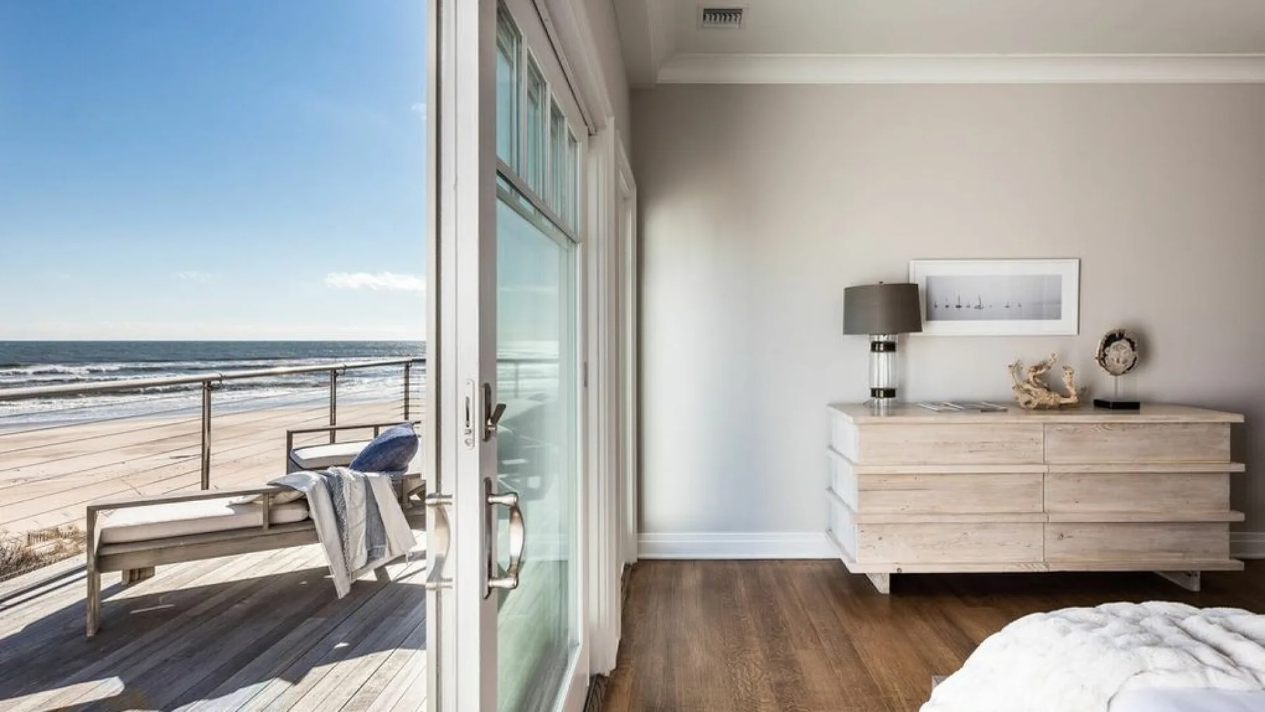 Un dormitorio se abre a una terraza junto al mar, con una cómoda junto a la puerta de vidrio.