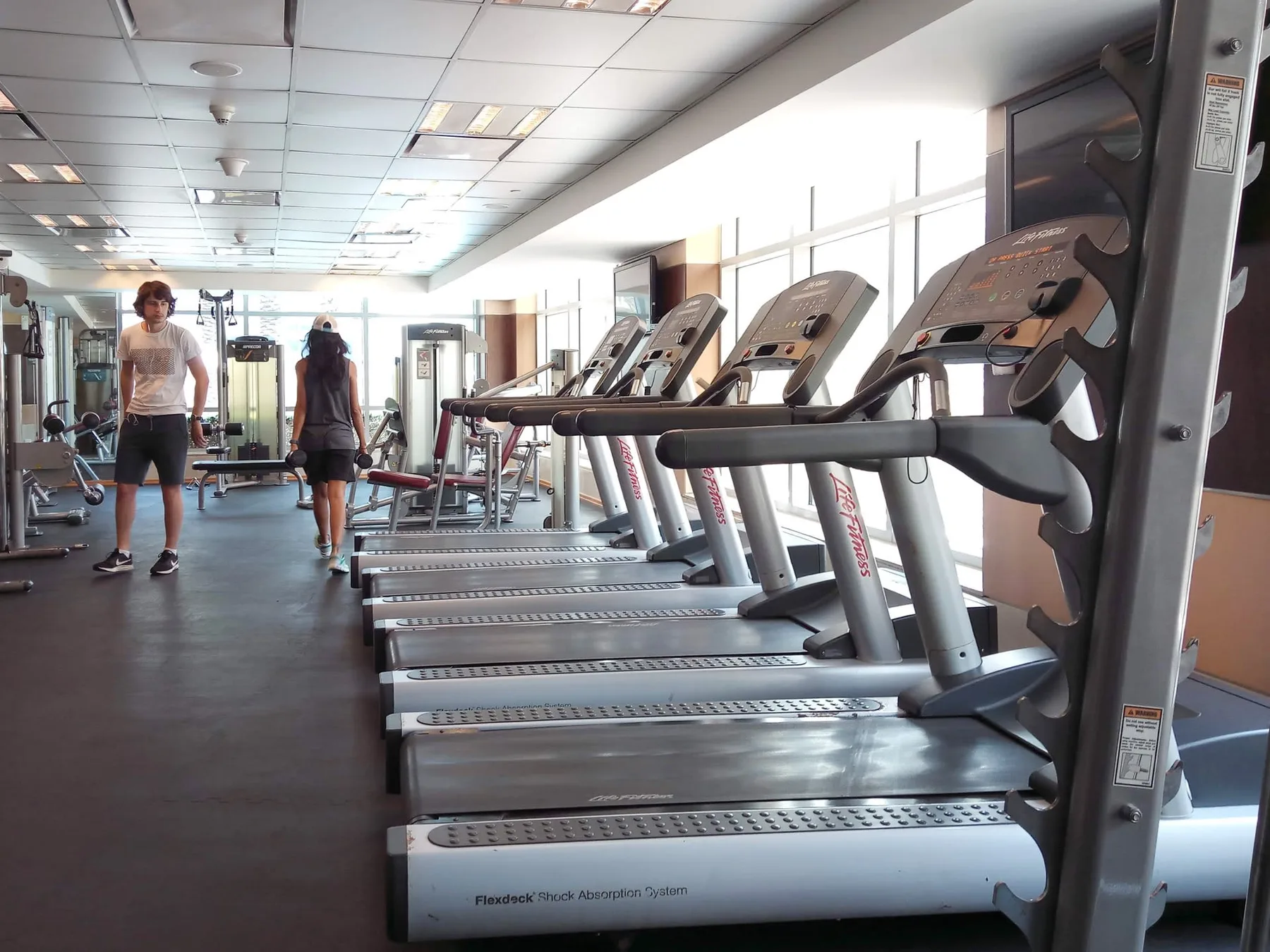 Un gimnasio con una fila de cintas de correr y equipos de ejercicio.