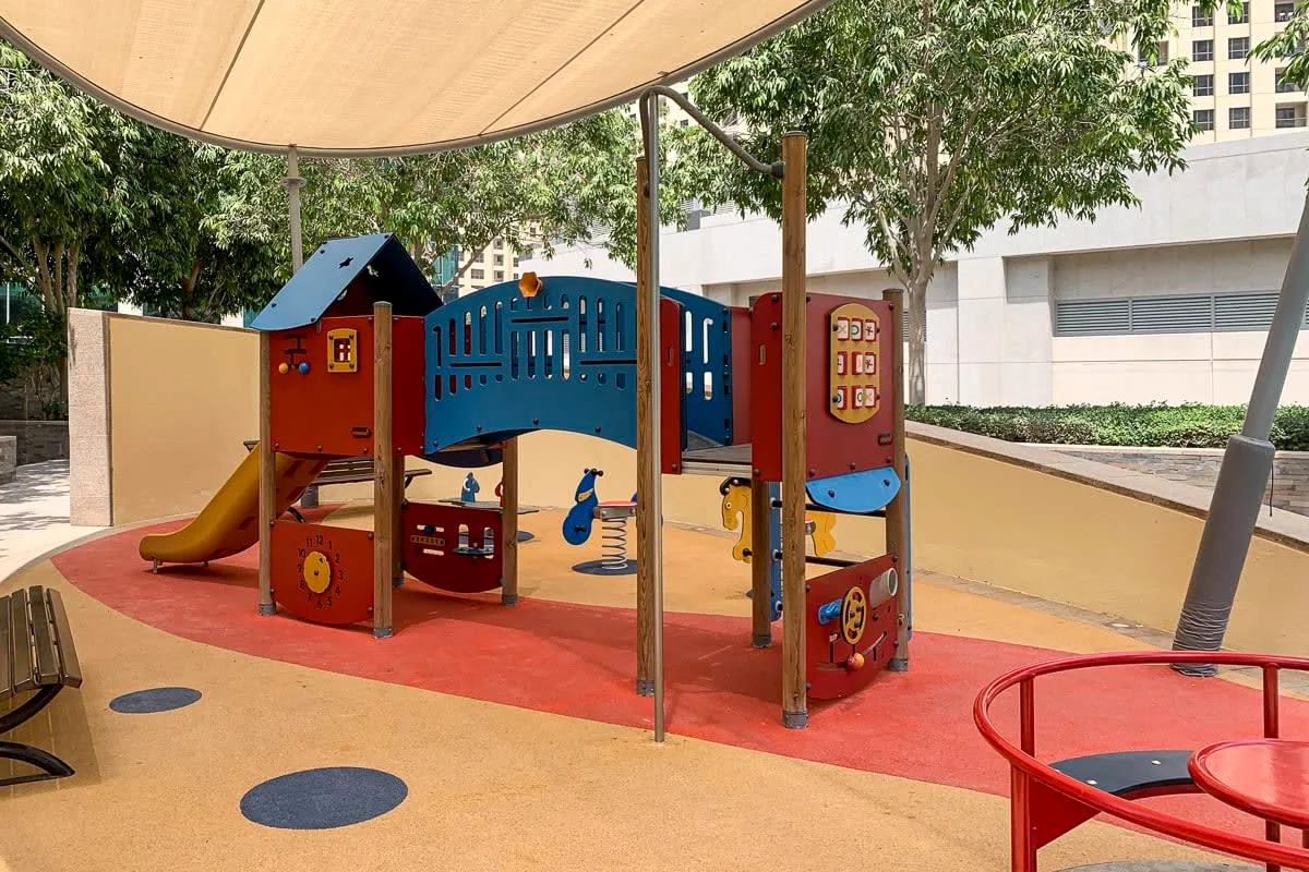 Una colorida estructura de juegos está bajo una cubierta de sombra en un área de juegos al aire libre.