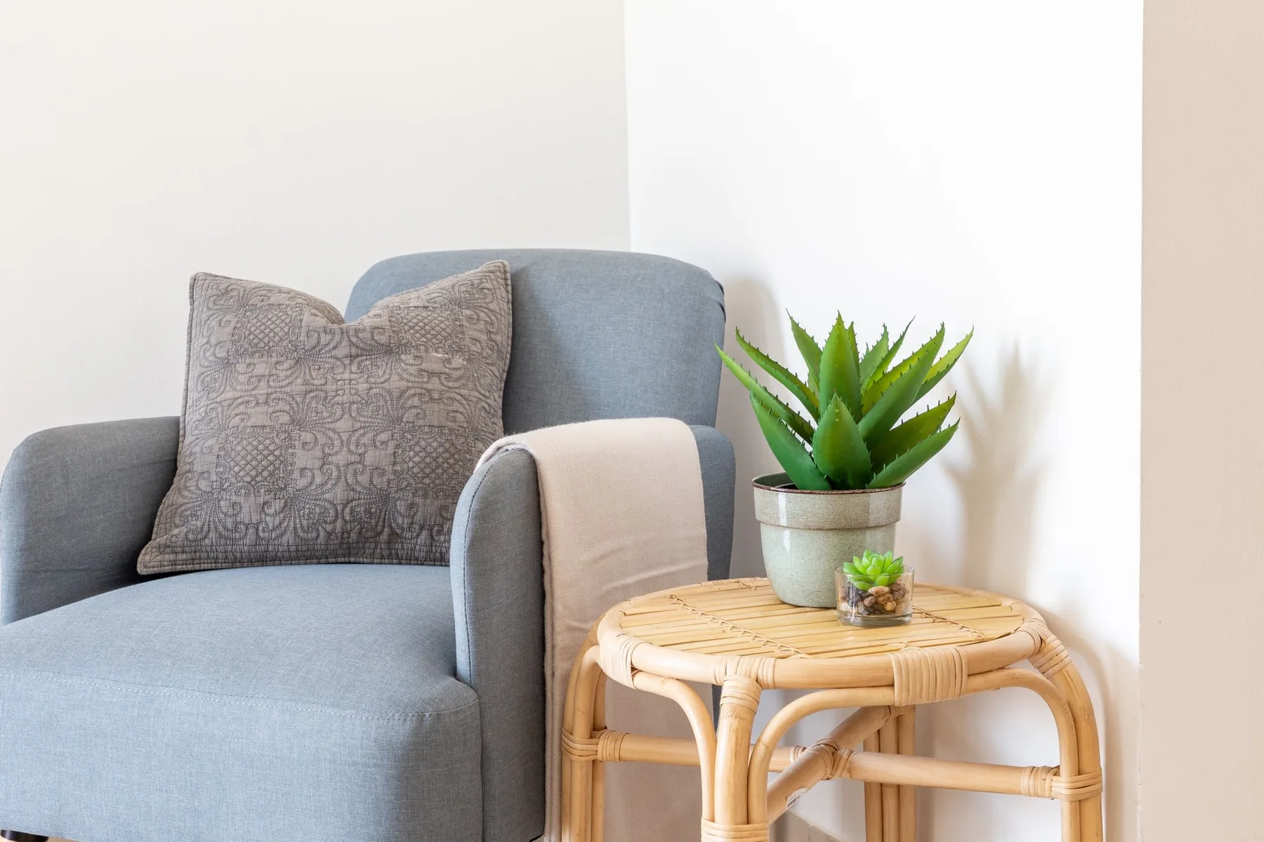 Un sillón tapizado azul está junto a una mesita redonda con una planta en maceta.