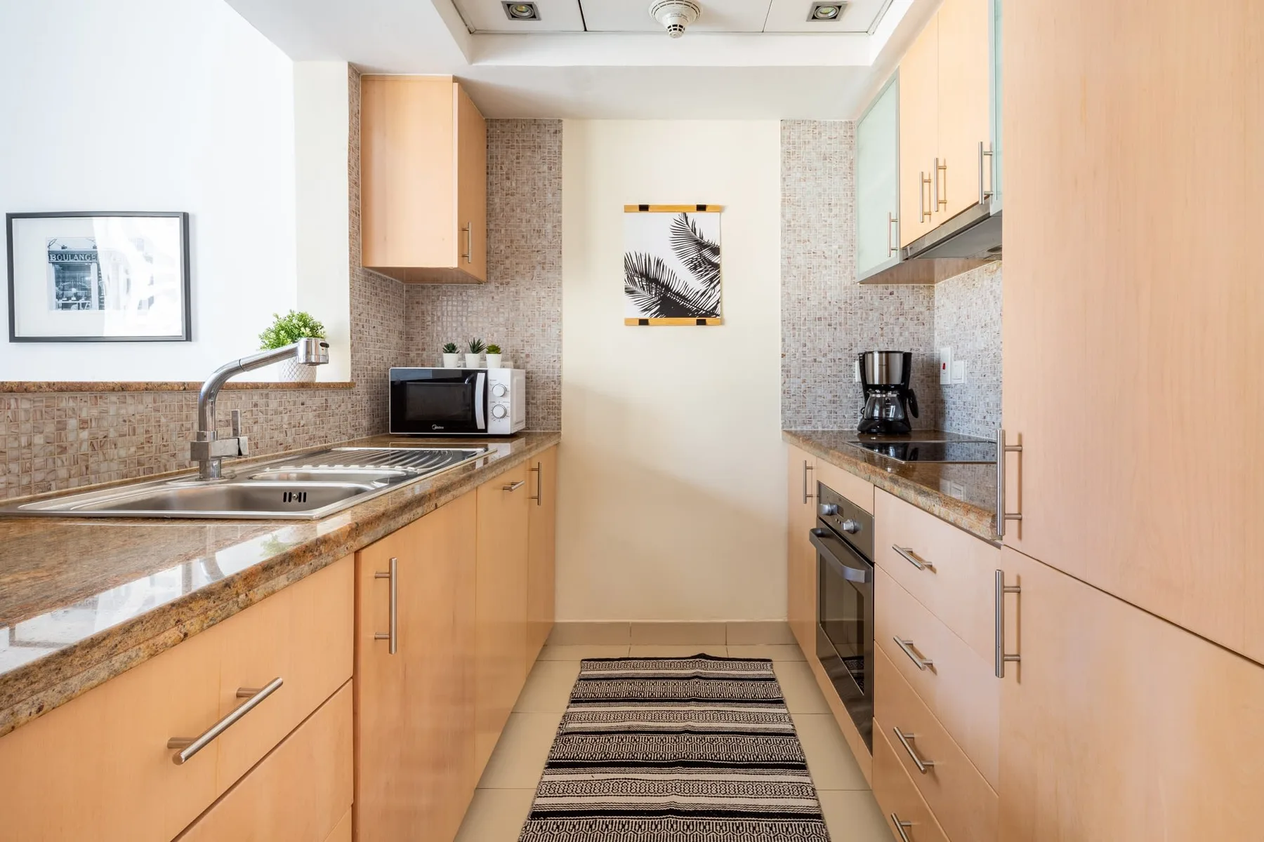 Una cocina luminosa en forma de pasillo con gabinetes de madera, fregadero y electrodomésticos sobre la encimera.