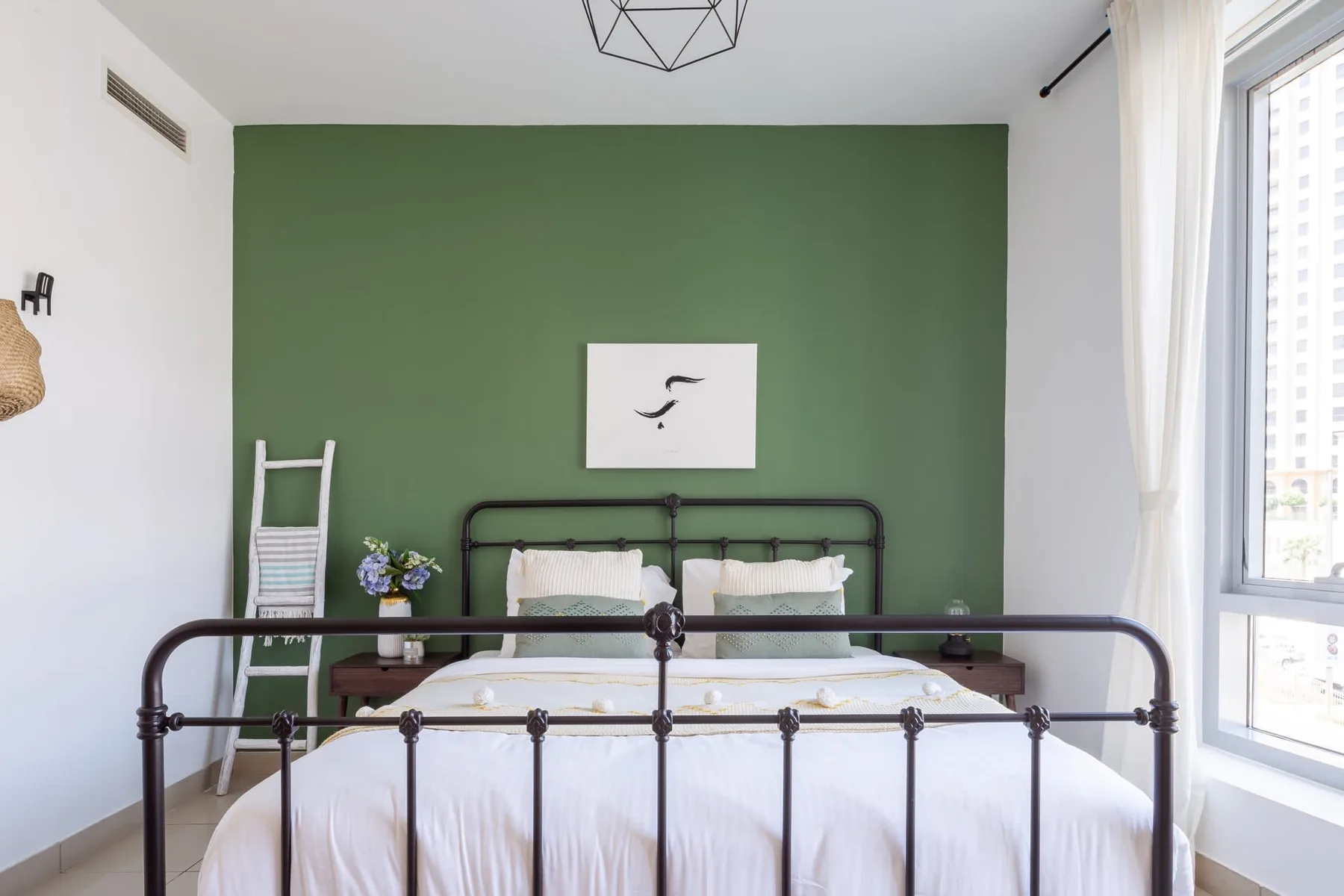 Un dormitorio con una cama de metal, ropa de cama blanca y una pared verde.