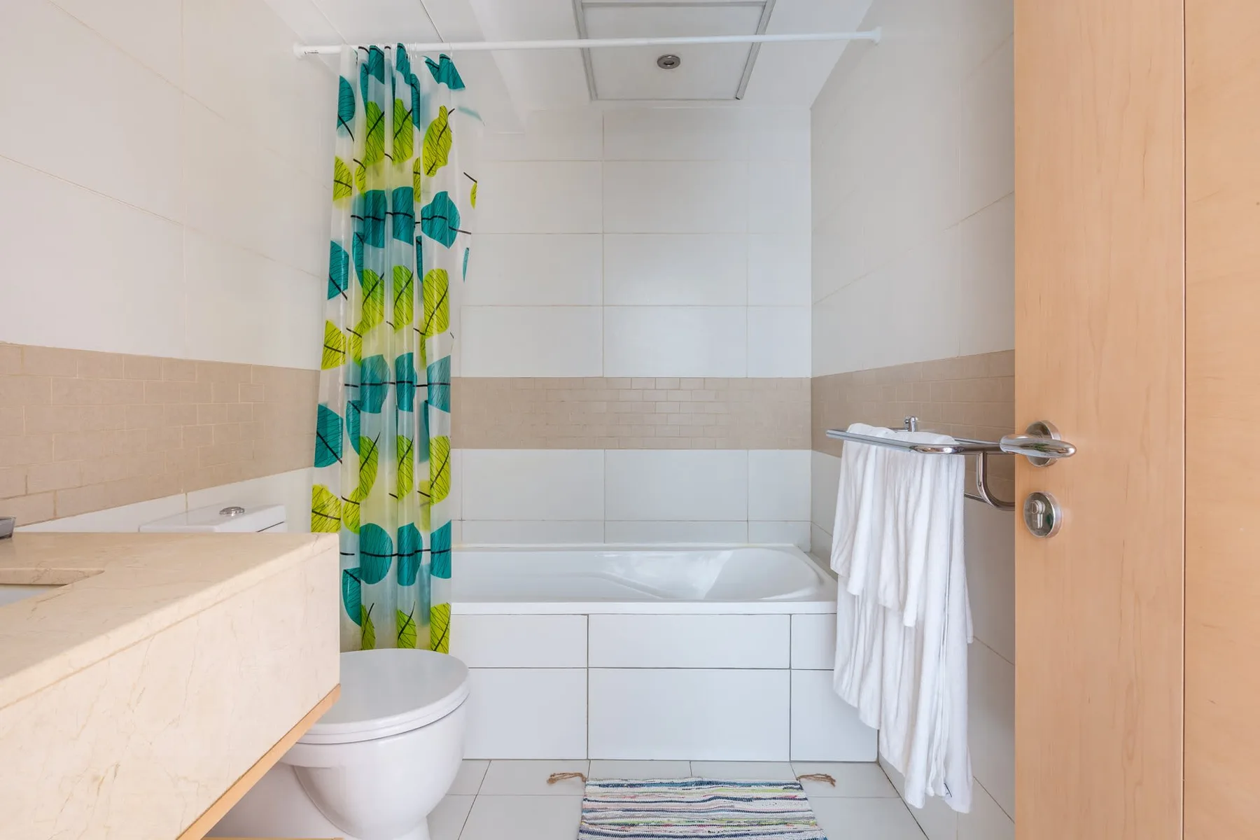 Un baño alicatado con bañera, inodoro y cortina de ducha estampada.
