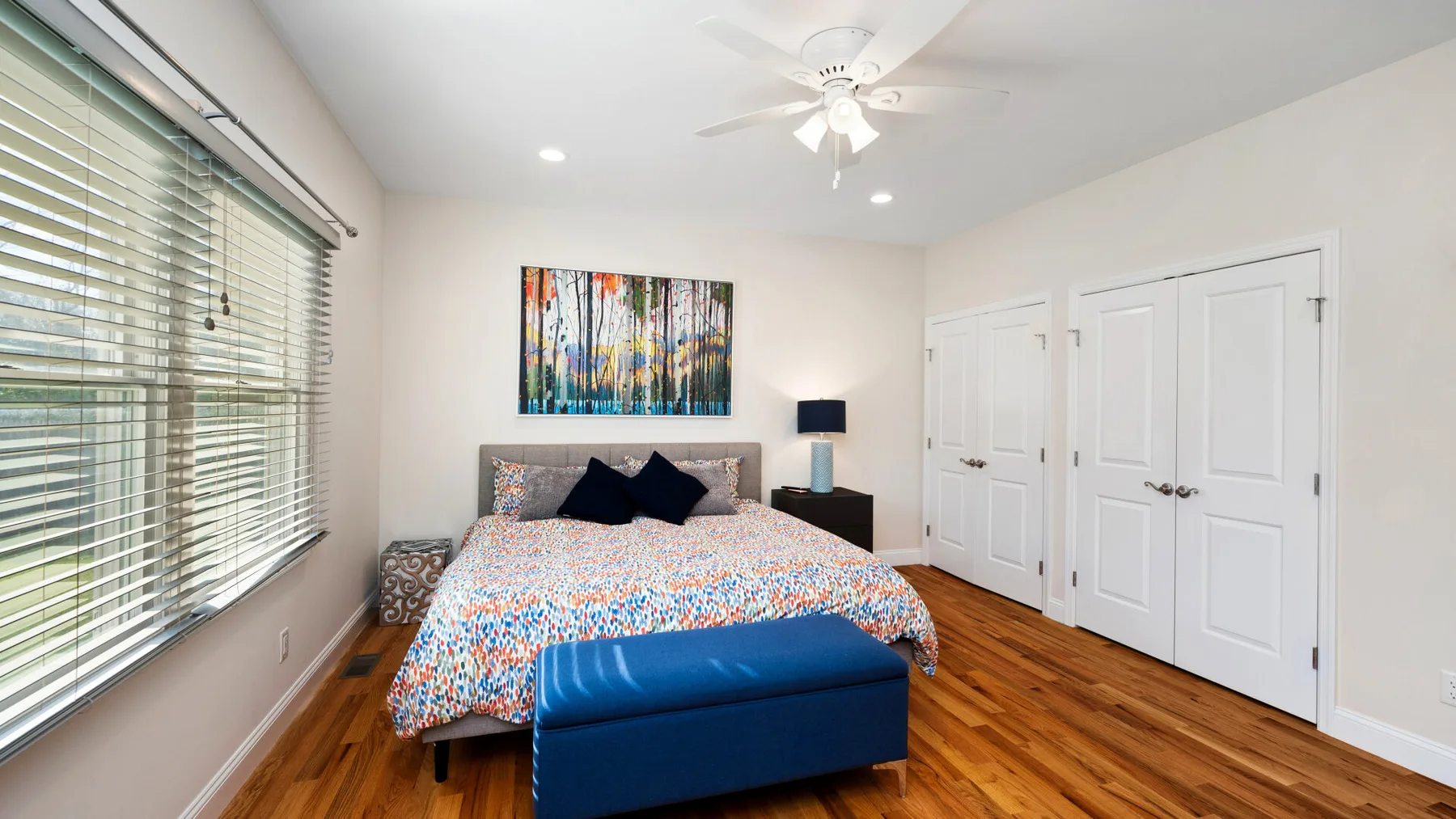 Un dormitorio con una cama, arte colorido en la pared y un banco azul.