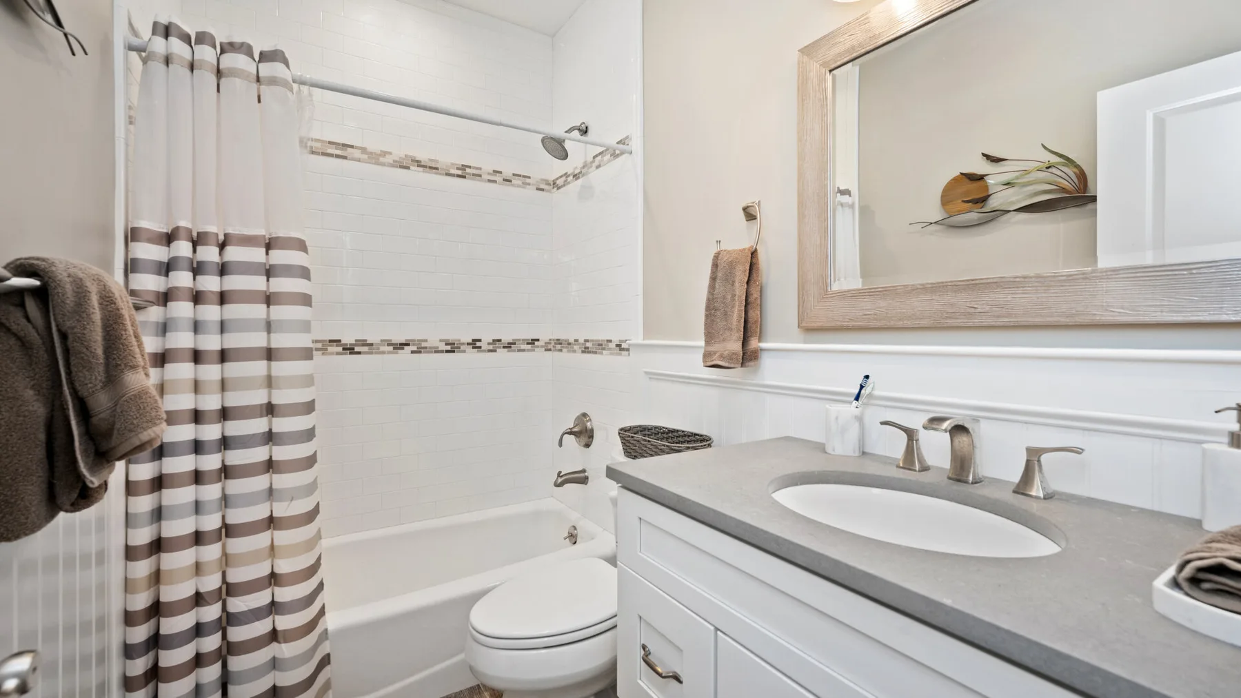 Un baño con bañera, cortina de ducha a rayas y tocador con lavabo.