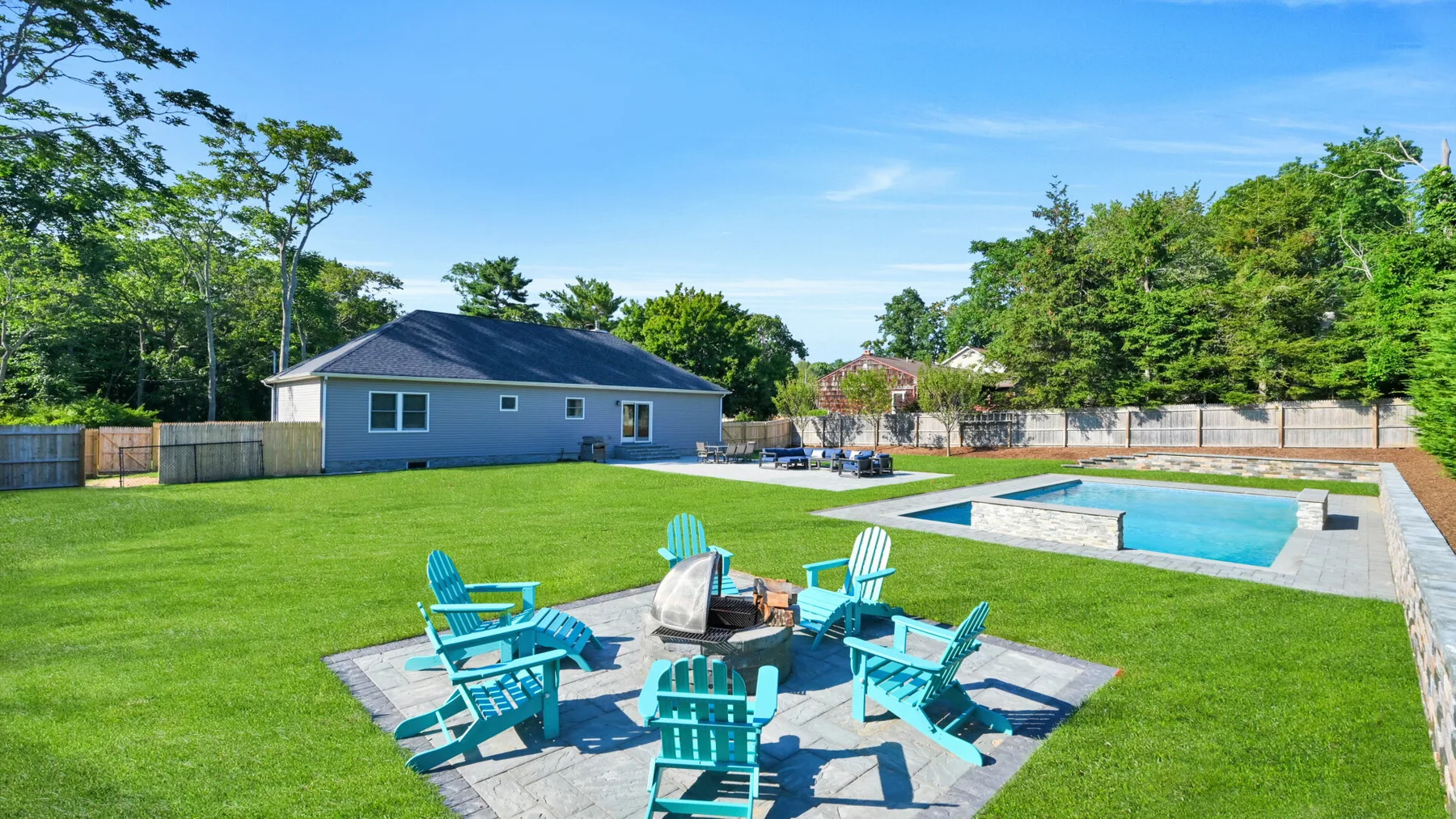 A grassy backyard has a patio seating area and an outdoor swimming pool.