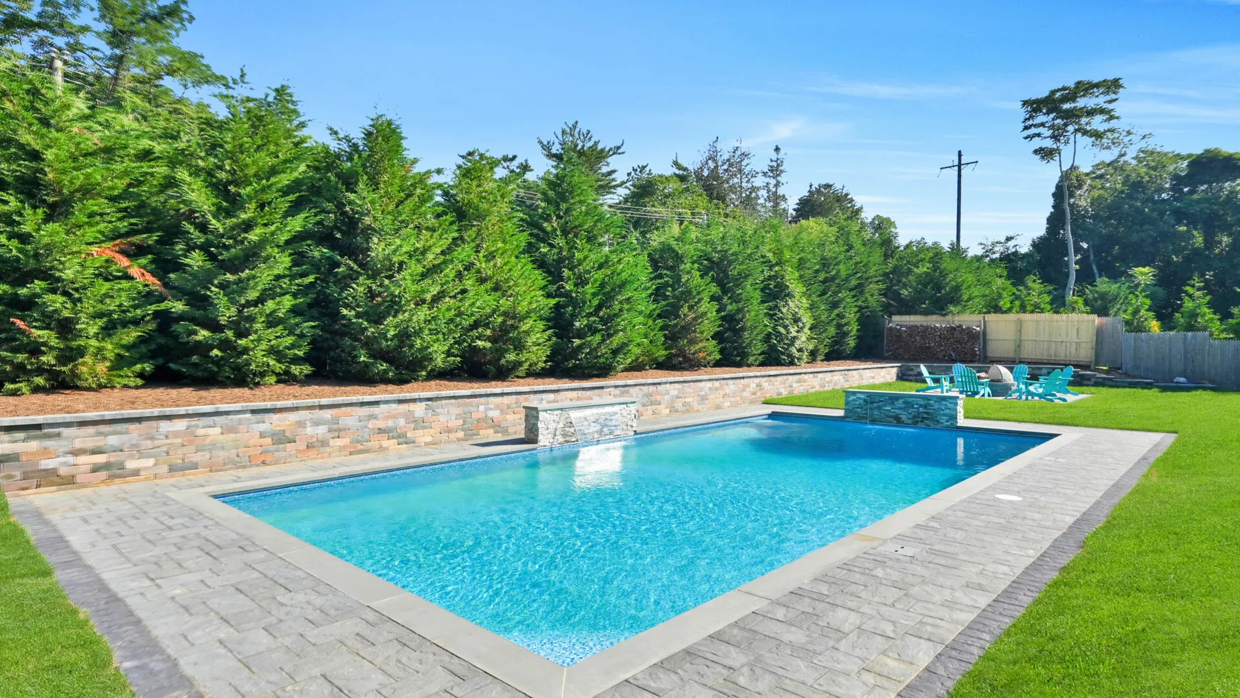 Una piscina rectangular está junto a una zona pavimentada y un césped verde.