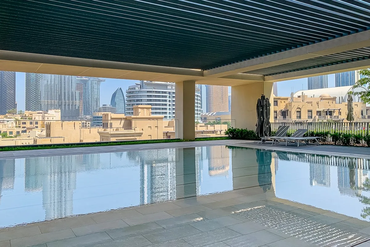 Una piscina en la azotea refleja los edificios de la ciudad bajo una cubierta sombreada.