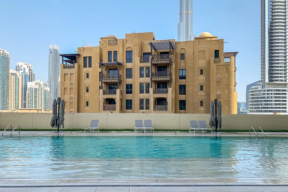Una piscina en la azotea se encuentra frente a un edificio de apartamentos beige y el horizonte urbano.