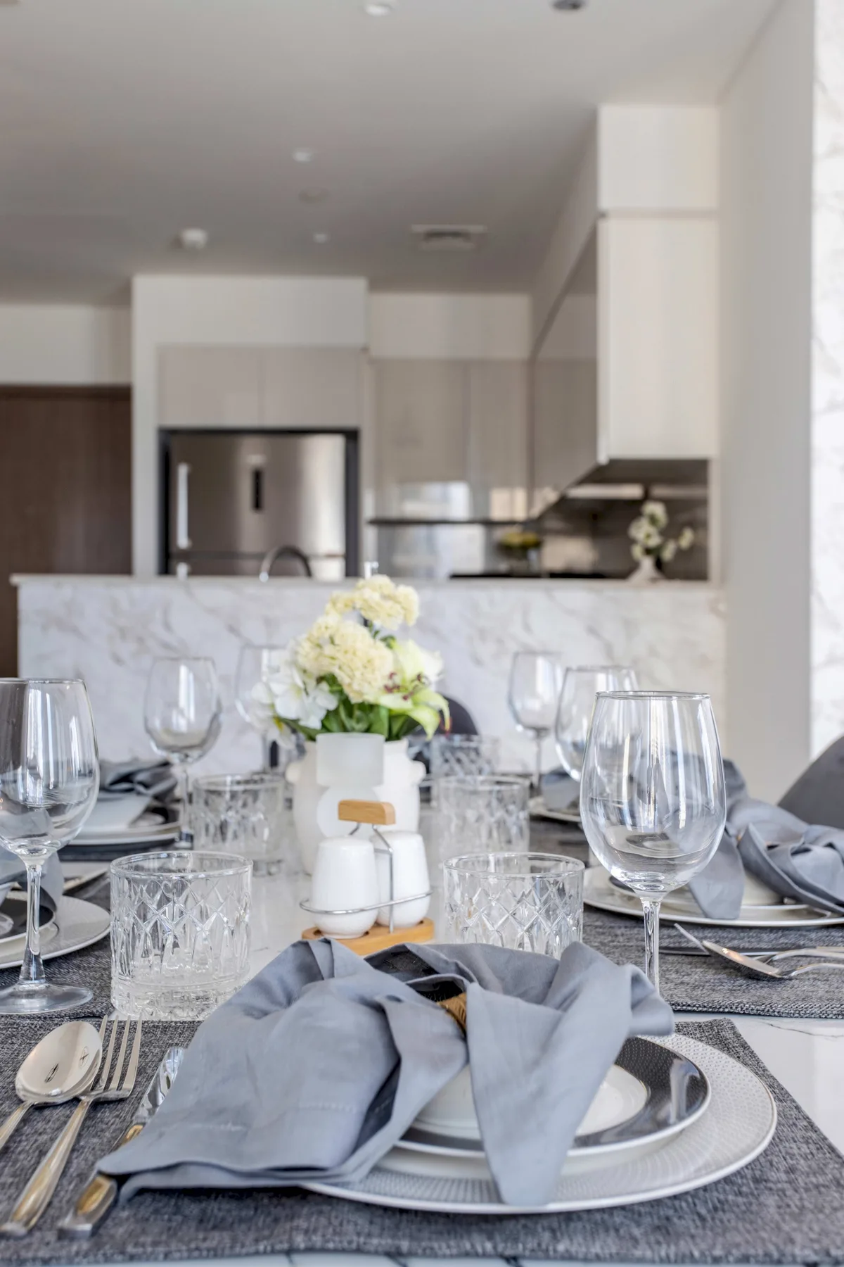 Una mesa de comedor está puesta con platos, vasos, servilletas dobladas y flores.