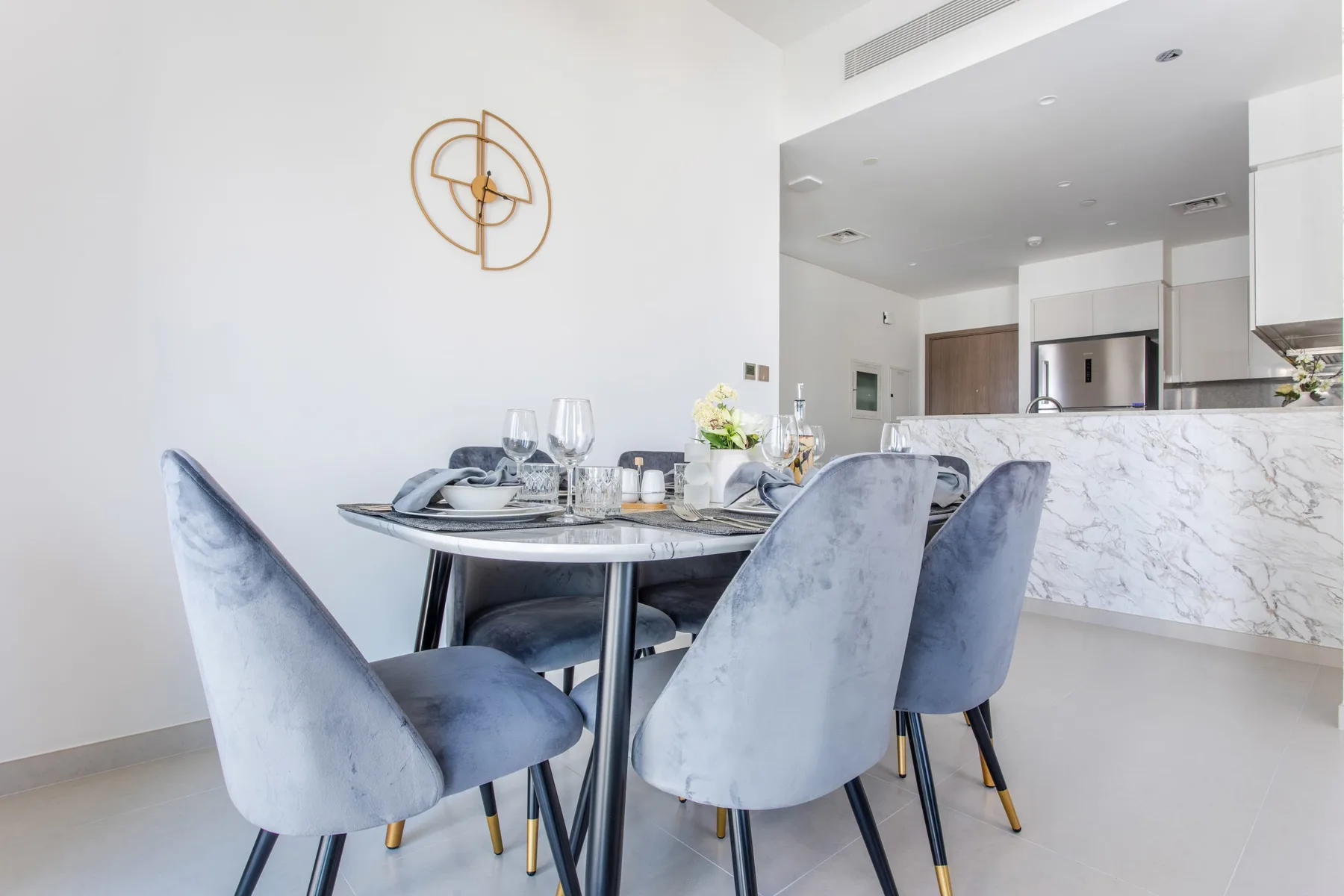 Comedor con asientos tapizados alrededor de una mesa puesta, junto a una cocina abierta.
