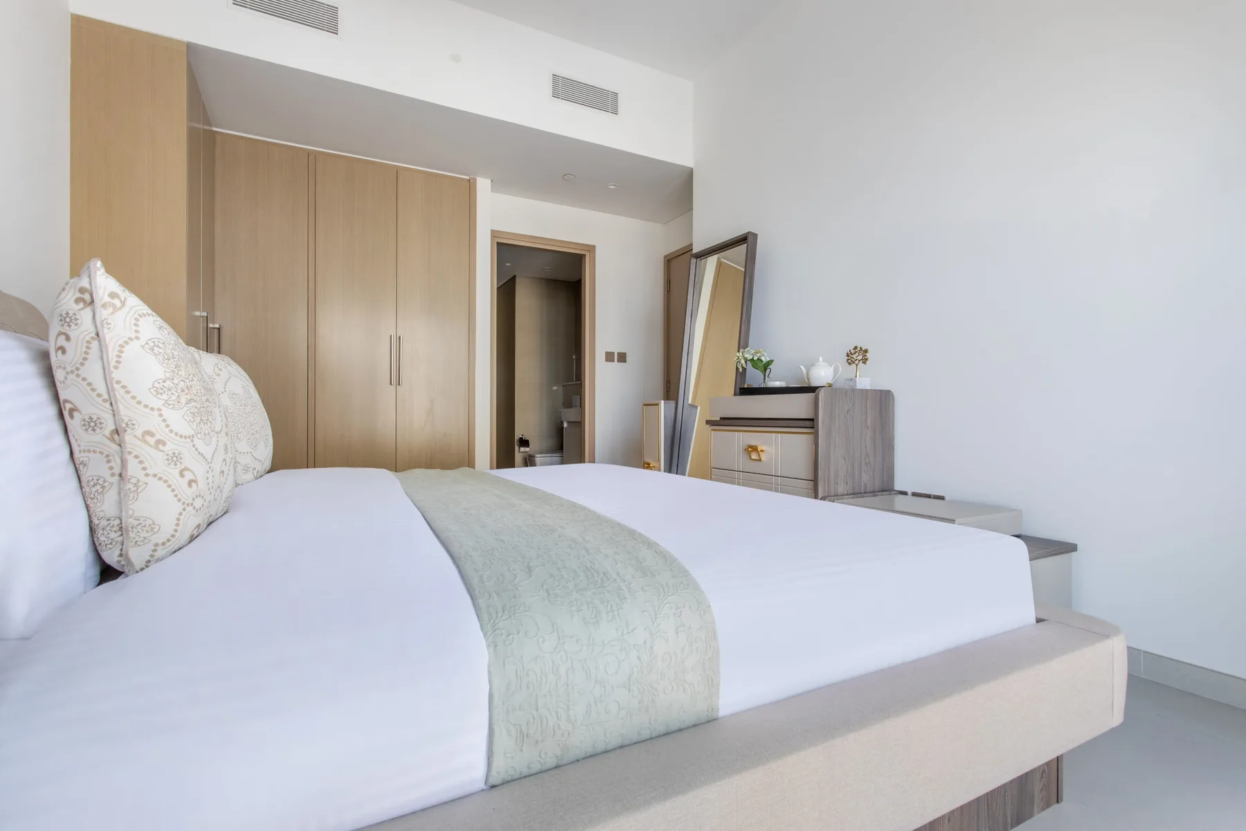 Un dormitorio luminoso con una cama bien hecha y armarios de madera clara.
