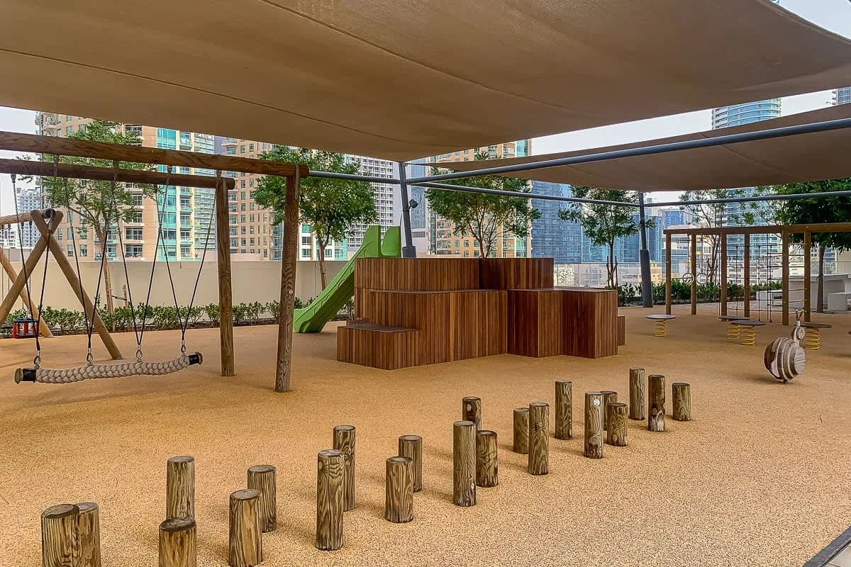 Un parque infantil al aire libre con estructuras para trepar y una zona de juego sombreada.