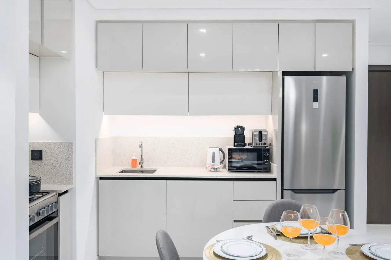 Una cocina moderna y luminosa con gabinetes blancos, electrodomésticos de acero inoxidable y una mesa de comedor.