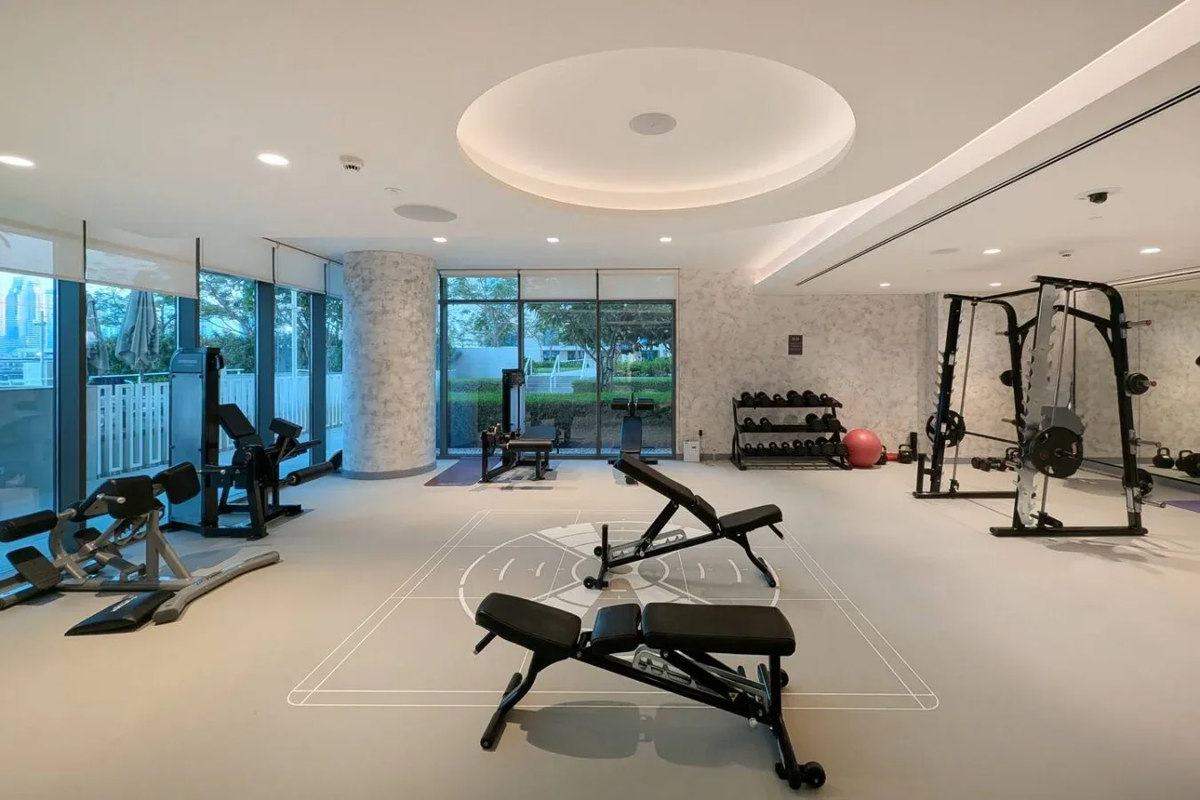 Un gimnasio interior luminoso con bancos de ejercicio, máquinas y grandes ventanales.