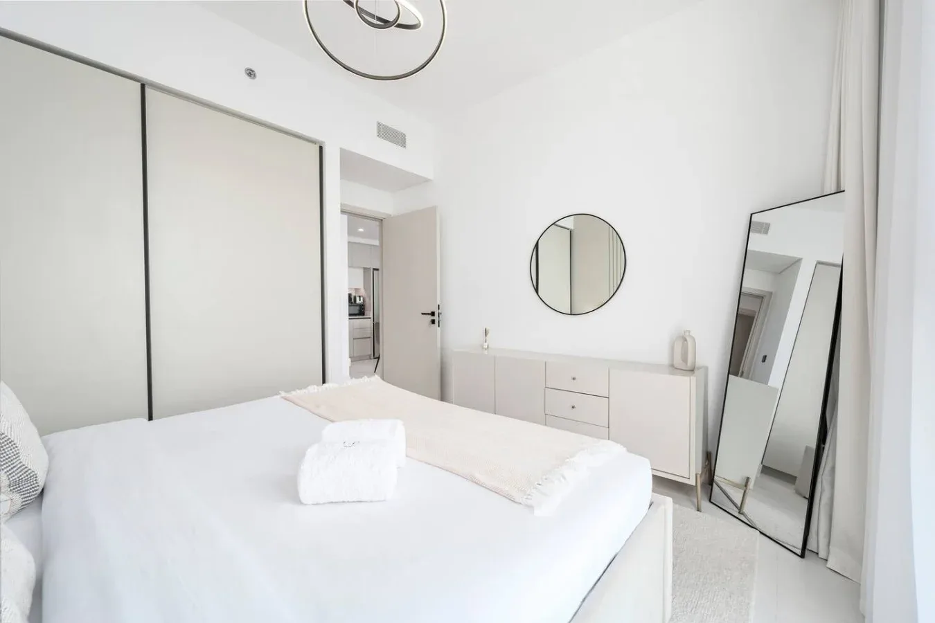 Un dormitorio luminoso con una cama bien tendida y un espejo redondo en la pared.