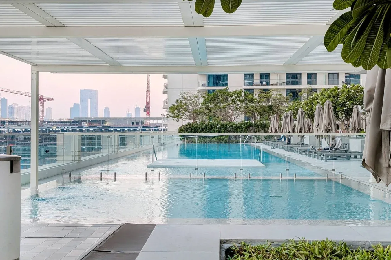 Una piscina en la azotea con barandillas de vidrio y edificios al fondo.
