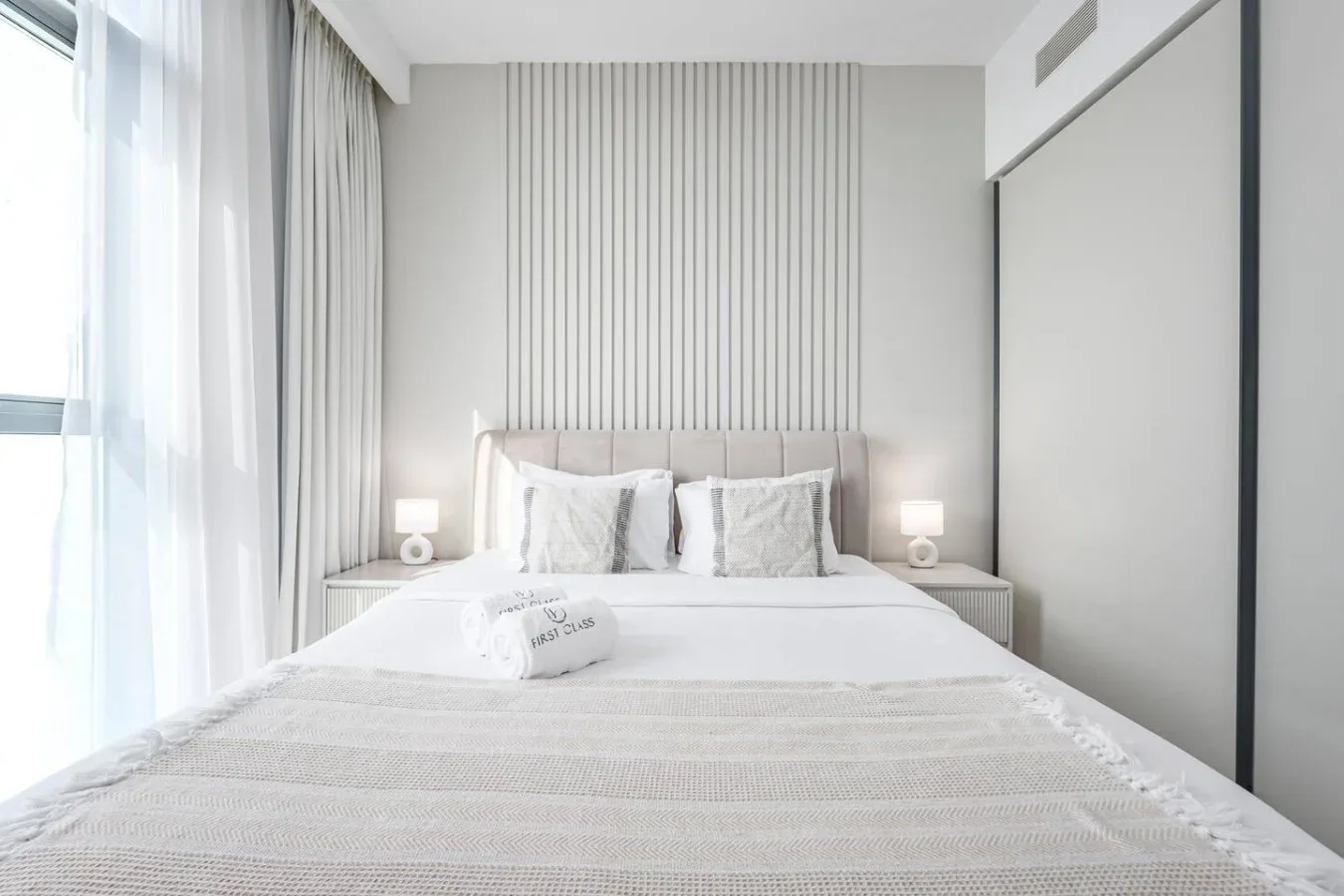 Un dormitorio luminoso con una cama bien hecha y cortinas translúcidas junto a la ventana.