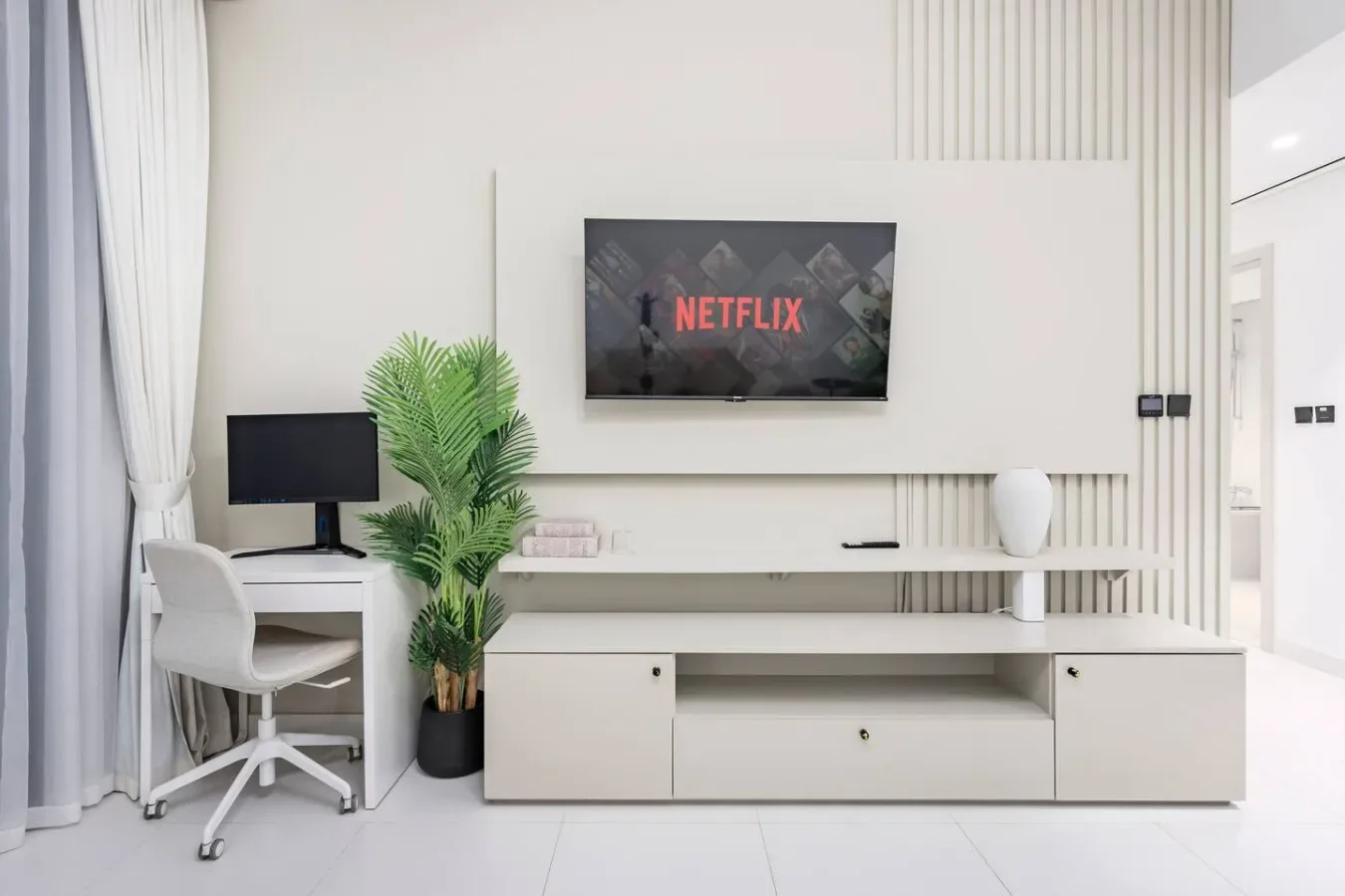 Una sala luminosa tiene un televisor montado en la pared sobre un largo mueble multimedia.