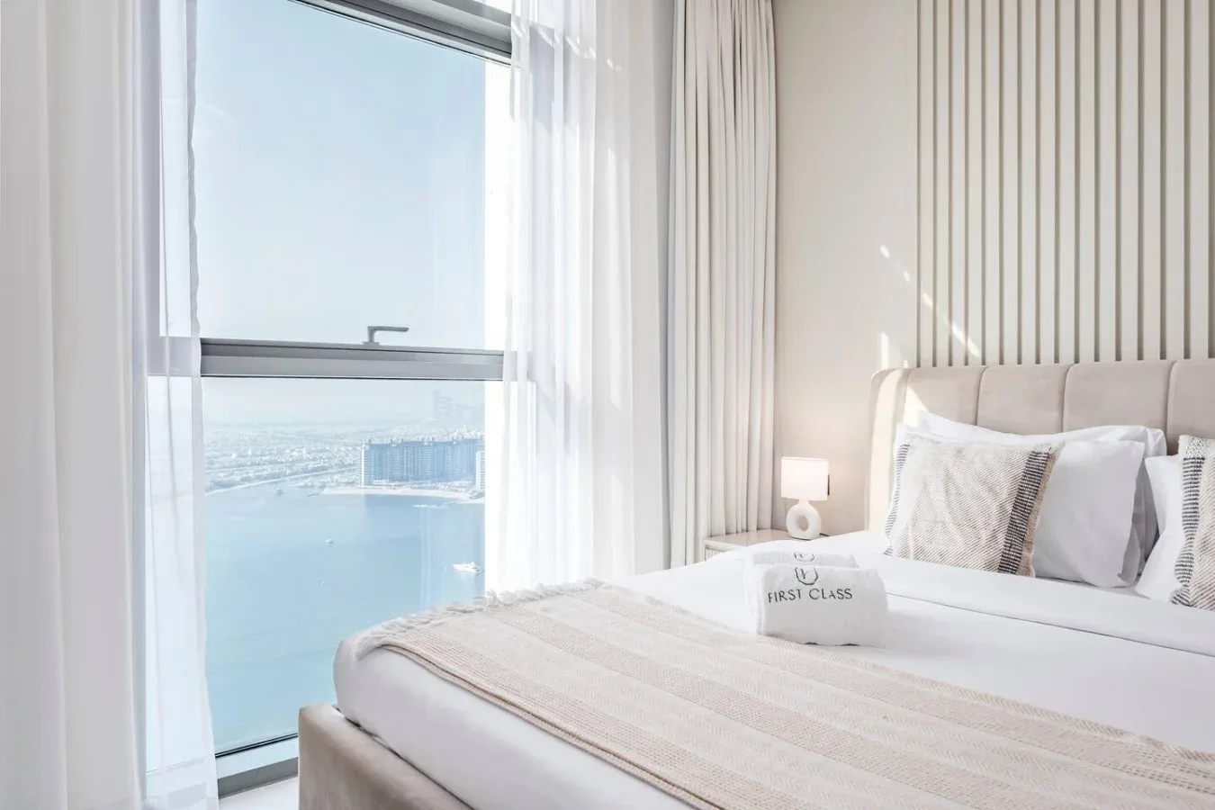 Un dormitorio luminoso con una cama bien tendida junto a una gran ventana con vistas al agua.