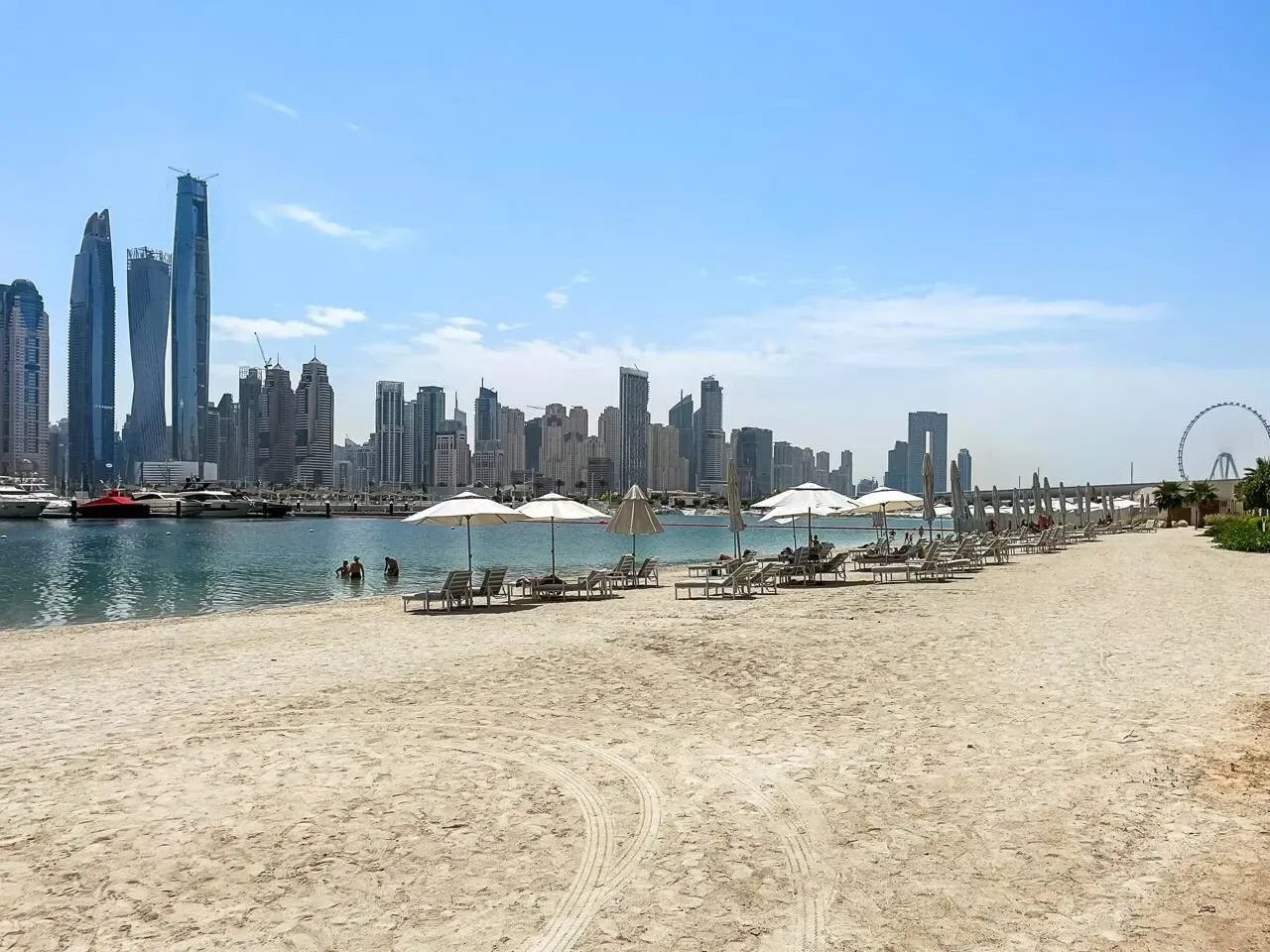 Una playa de arena da a aguas tranquilas y un horizonte urbano distante.