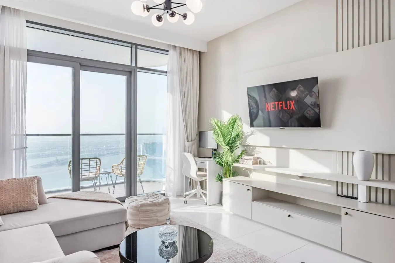 Una sala luminosa tiene televisión, asientos y puertas de vidrio que dan a un balcón.